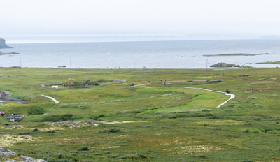 View across site Reconstruction on middle left; Ruins in grass, L'Anse aux Meadows, Newfoundland, Canada, August 2022